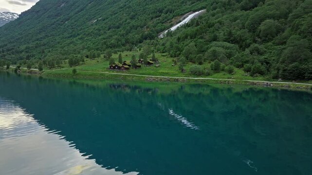Aerial view over deep blue Lovatnet Lake, Loen Valley, Norway. Forested slopes and mirror-like water create a tranquil alpine atmosphere.