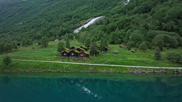 Breng Seter summer farm beside Lovatnet Lake in Loen Valley, Norway. Traditional wooden buildings sit in lush meadows beneath forested slopes.