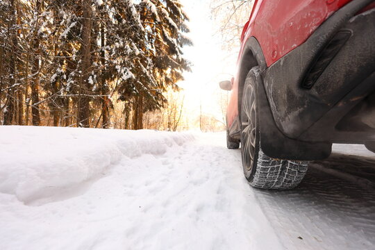 Low-angle shot of a red SUVs winter tire on a snowy forest path, sunlit pines, deep snow, and rugged treads evoke quiet winter travel and seasonal resilience.