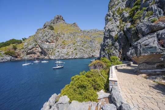 Path along the coast, sailing boats in the bay near Torrent de Pareis, Sa Calobra, Majorca, Balearic Islands, Spain