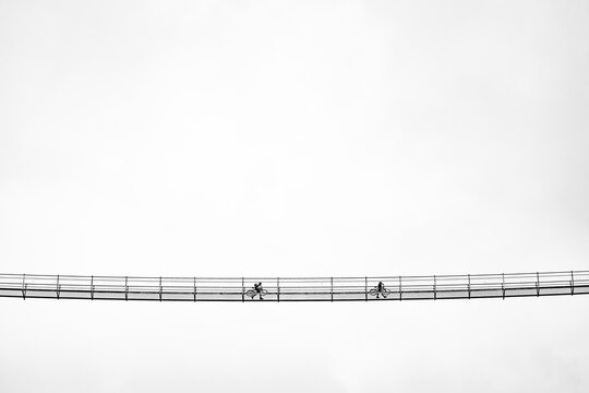 Suspension bridge with two cyclists against a white sky, Bach, Lechtal, Tyrol, Austria