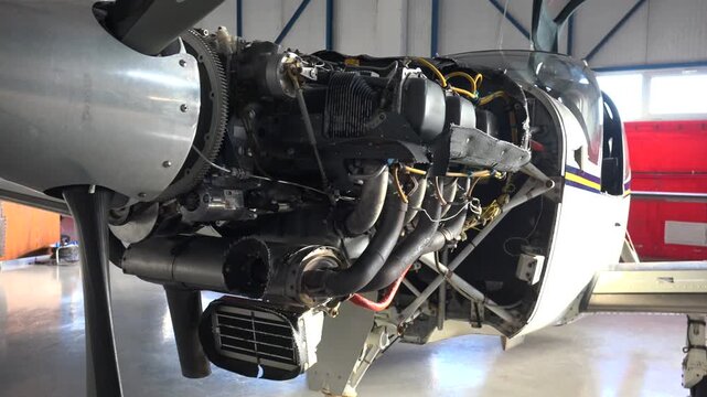 Single engine propeller airplane undergoing maintenance repair inside aircraft hangar facility. Exposed motor components show technical service work on a training aircraft during repair.