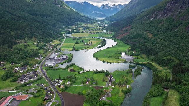 Wide drone panorama of Stryn landscape and river bends. Calm, scenic view of rural Norway with fields, houses, and flowing water framed by steep forested slopes.