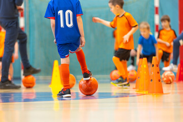 Naklejka premium Football training for children. Indoor soccer young player with a soccer ball in a sports hall. Sport background.