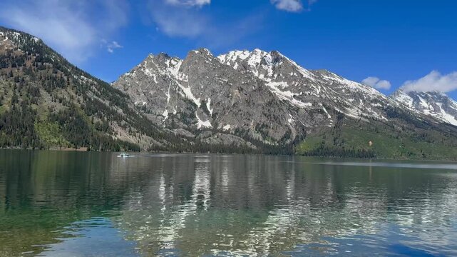 Scenic view of snow-capped mountains and the still waters of Jenny Lake in the Grand Teton National Park. Panning left to right.