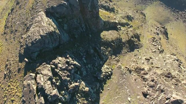 Aerial view of rocky barren mountain ridge with stony slopes and treeless snowless peak. Overhead landscape shows dry rugged terrain, steep cliffs, and exposed geology under clear sunlight.