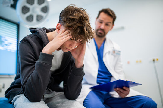 Depressed teenage patient sitting on hospital bed, talking with caring doctor.