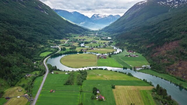 Drone panorama of a wide river bend and cultivated fields in Stryn, Norway. Peaceful daylight scene highlights agricultural patterns and surrounding mountains.