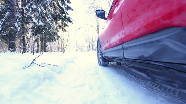 Low-angle shot of a red SUVs tire gripping a snowy forest track, sunlit evergreens, deep snow, and winter road traction evoke quiet adventure and seasonal resilience.