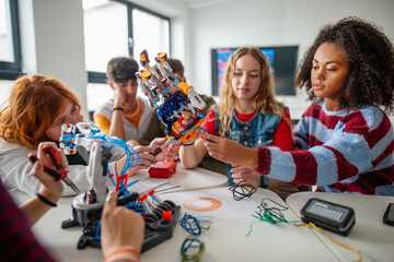 Team of teenagers assembling robotic arm in technology class.