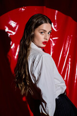 Naklejka premium Young woman in stylish outfit stands confidently against a vibrant red background