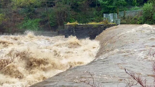 Torrent of water in a river flowing over a weir after heavy rain from a storm. 