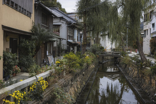 Shimoda, Japan - 25 November 2025: View of a tranquil canal reflecting the quaint architecture, lush greenery, and the gentle arch of a small bridge.