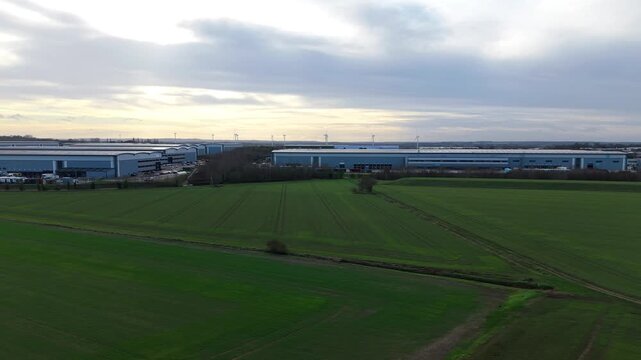Biggleswade, United Kingdom - 24 January 2026: Aerial view of multiple warehouses contrasting with vibrant green fields under a cloudy sky, showcasing industrial and rural harmony.