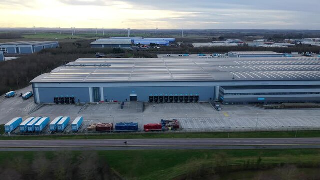 Biggleswade, United Kingdom - 24 January 2026: Aerial view of a large warehouse with rows of containers and loading docks, under a cloudy sky.