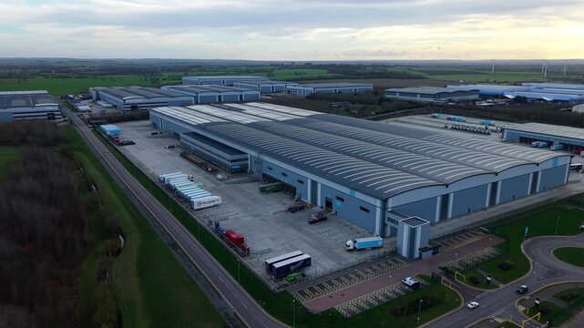 Biggleswade, United Kingdom - 24 January 2026: Aerial view of a complex of warehouses, their roofs reflecting the sky, surrounded by green fields and infrastructure.