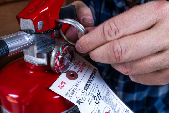 PROSPECT, OREGON &ndash; JANUARY 29, 2026: An illustrative editorial photo of a males hands inspecting a red fire extinguisher mounted to a wall to ensure safety compliance and expiration date.
