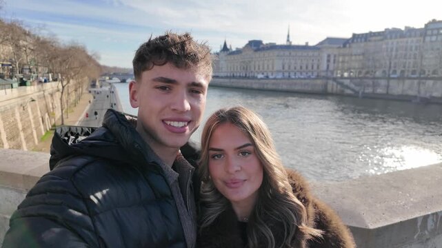 A couple in love takes candid selfies in Paris with the Seine River and Parisian architecture in the background The handheld POV shot captures their romantic getaway social media content travel vlogs 
