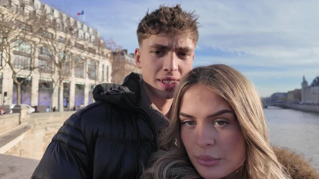 A young couple takes candid selfies in Paris France with the River Seine and city buildings in the background on a sunny day The footage is handheld POV social media content creation.