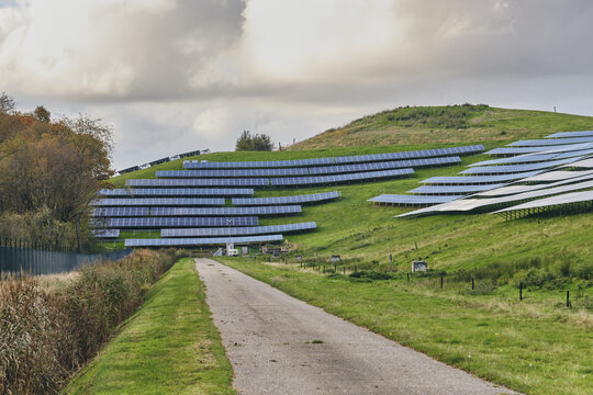 Wijster, Netherlands - 27 October 2024: View of solar panels arrayed on a landfill across the rolling green hills, contrasting sharply against the overcast sky.