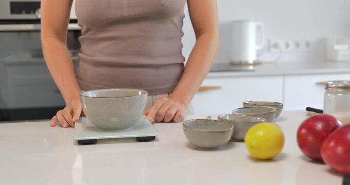 Woman adding flour into bowl on digital kitchen scale, precise ingredient measuring for baking