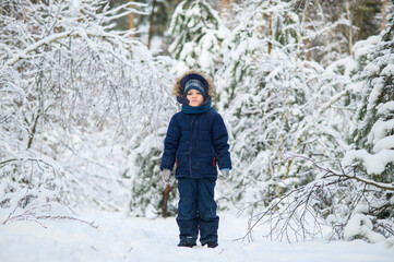 Little boy walking and playing in snowy winter forest. Natural childhood, winter season, outdoor lifestyle, family leisure, exploration and connection with nature.
