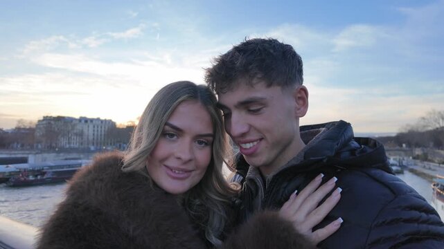 A couple in Paris is taking candid selfies on a bridge over the Seine River at sunset The video shows a handheld POV shot of the couple as they pose and smile for the camera creating social media cont