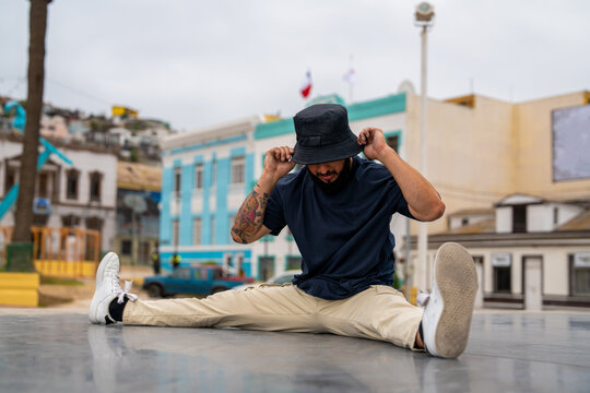 Man doing a split stretch while adjusting bucket hat in a city square