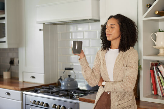 Young African woman drinking coffee with her eyes closed in her kitchen