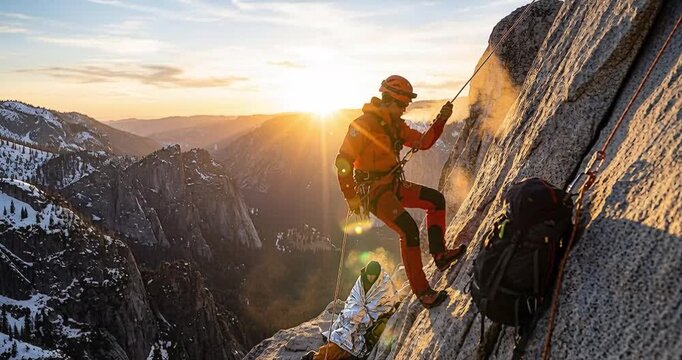 Mountain climber descending rocky cliff against golden sunset