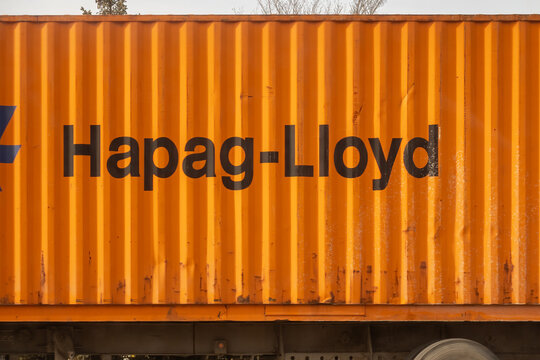 Calgary, Alberta, Canada. Feb 2, 2026. A bright orange Hapag-Lloyd shipping container being transported by a truck on a sunny day.