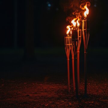 Multiple wooden torches burning brightly at night, casting warm, orange light over the dark ground and surrounding natural environment, intense, flicker, adventure