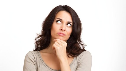 Fototapeta premium Thinking woman with long brown hair wearing a beige top, resting her chin on her hand and looking upward against a white background. Concept Thinking woman portrait, Long brown hair, Beige top