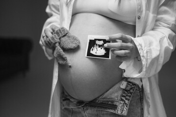 A pregnant woman holds an ultrasound image of her baby on her rounded belly. A tender and touching moment of anticipation