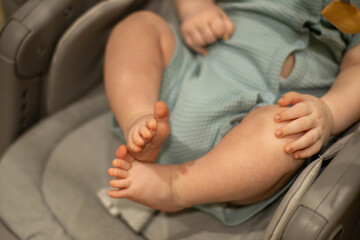 Close-up of a baby's feet resting in a car seat. The infant has chubby toes and soft skin, wearing a light blue outfit. The background is softly blurred.
