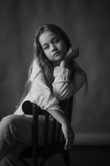 Black and white studio portrait of a girl in a pensive mood, sitting on a chair