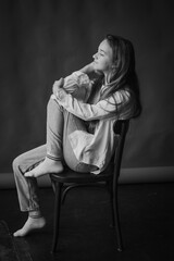 Black and white studio portrait of a girl in a pensive mood, sitting on a chair