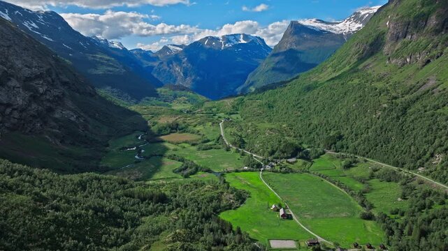Aerial view over a wide Norwegian valley in Norway, with patchwork farmland and a river winding between steep green mountains. Bright daylight emphasizes the depth of the valley and classic Norwegian.