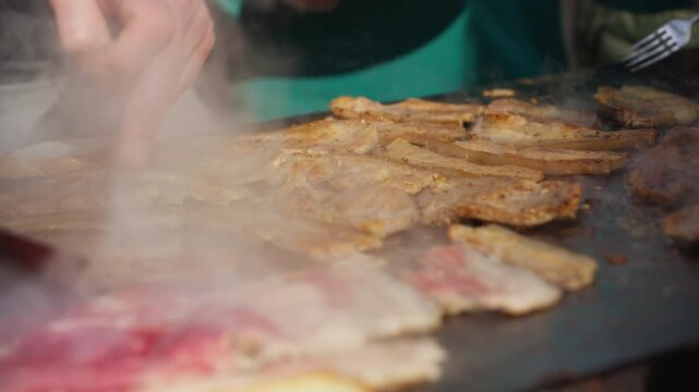 Simple comfort food being cooked on flat grill outdoors. Warm tones, sizzling meat, and relaxed atmosphere of casual street dining.