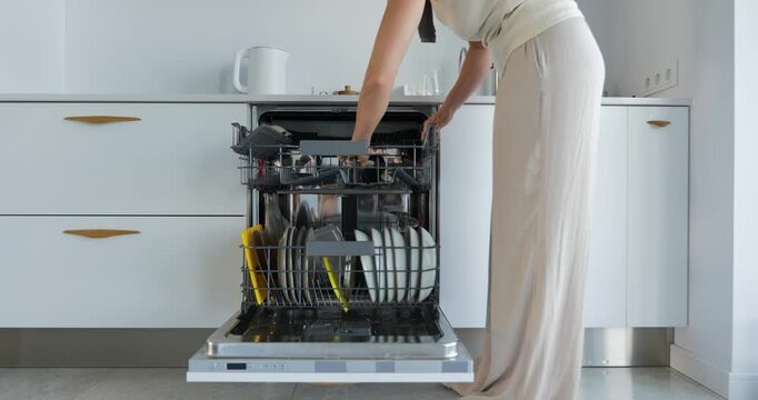 Woman loading dishes into dishwasher in modern kitchen