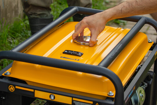 A close-up of a hand opening the lid of a yellow portable generator. The generator sits on a grassy surface, revealing its sturdy construction.