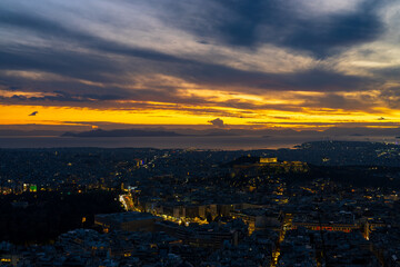 Fototapeta premium Panorama of Athens at sunset with a view of the Acropolis. The city lit up at night against the backdrop of enchanting clouds and a mesmerizing sunset. A peaceful picture of relaxation 