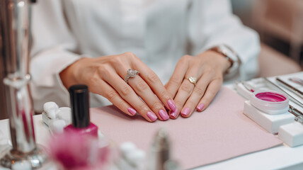 Obraz premium A woman seated at a manicure station receiving a pink nail treatment, detailed view of hands and salon tools