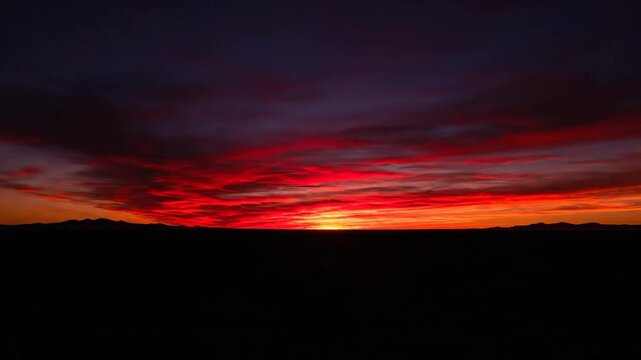 Vivid vermilion sunset bleeding into a dramatic horizon, painting the evening sky with fiery clouds and silhouettes of distant mountains