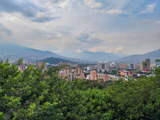 A city view set against mountains, featuring a mix of high-rise buildings, commercial blocks and lush greenery on rolling hills. Ideal for urban life, travel and landscape themes.
