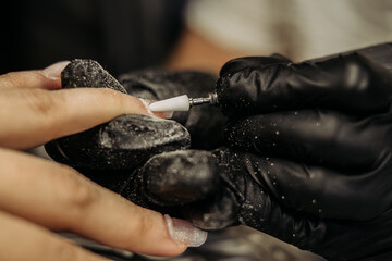 Hardware manicure procedure: a technician wearing gloves treats the nail with a professional instrument.