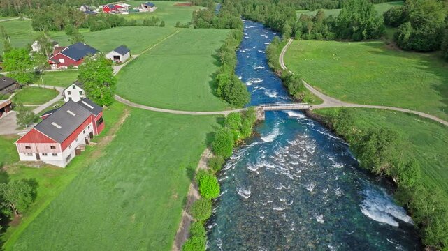 Aerial drone view of the Gudbrandsjuvet river in Norway passing under a small bridge.Drone view downstream reveals fields, paths, and the river dividing the landscape.