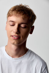 Fototapeta premium Young man with closed eyes and peaceful expression wearing a white tee, soft studio lighting enhances calm mood and serenity, minimal background highlights contemplation and inner peace in a clean,