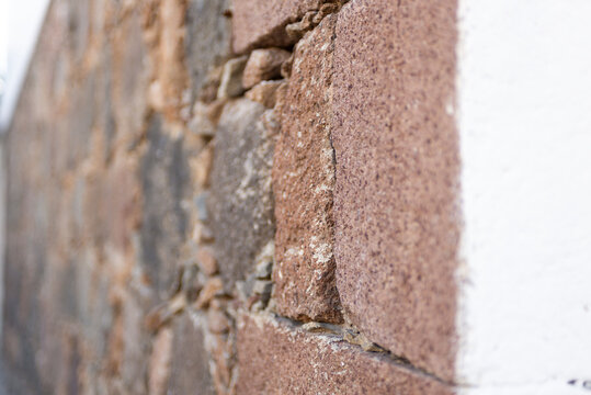 Close-up of a rustic stone wall with roughly hewn stones in reddish-brown tones. Angled view.