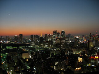 Fototapeta premium Tokyo skyline at dusk with illuminated buildings and orange sunset sky
